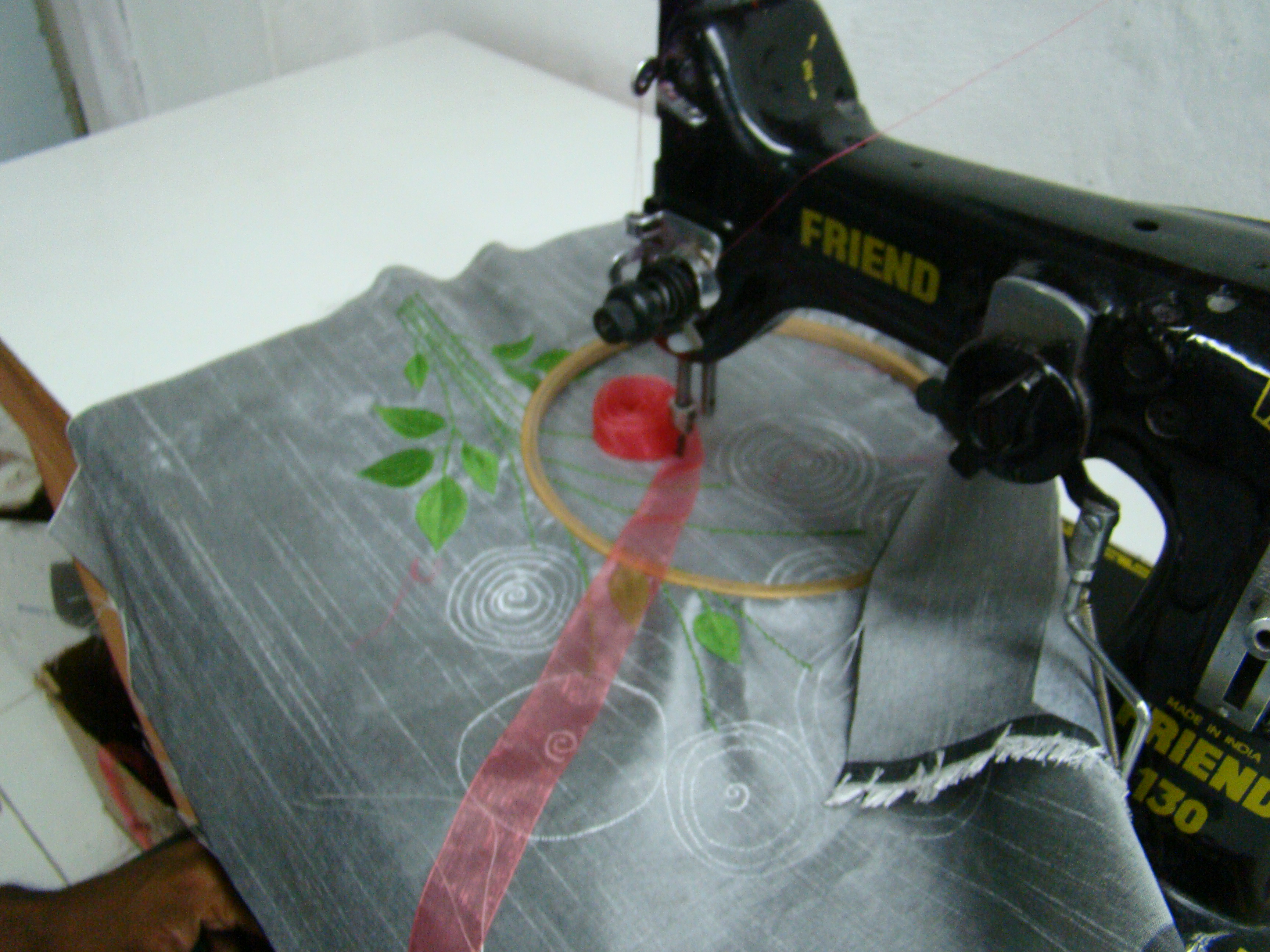 An embroidery hoop on the machine, mid-stitch on a rose pattern.