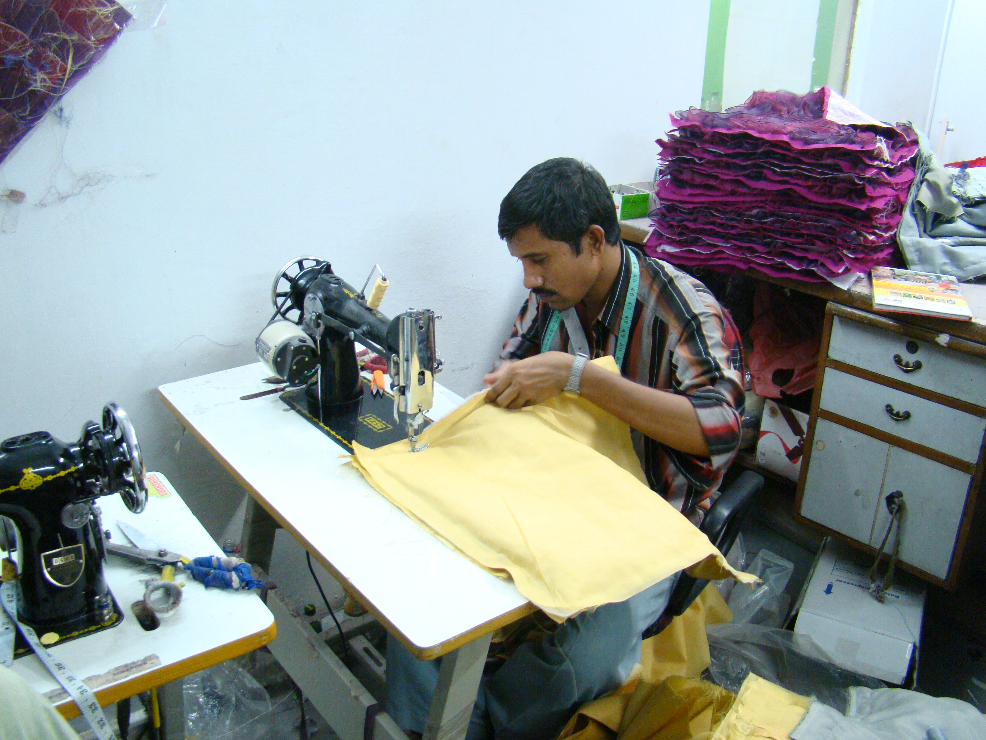 An artisan at a sewing machine working on a magenta cover, with finished covers stacked nearby.