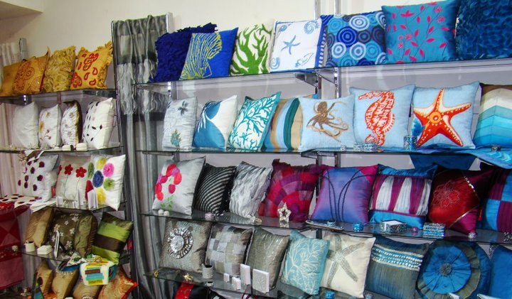 Showroom shelves with blue, cyan and silver pillow covers featuring starfish, coral and shell motifs.