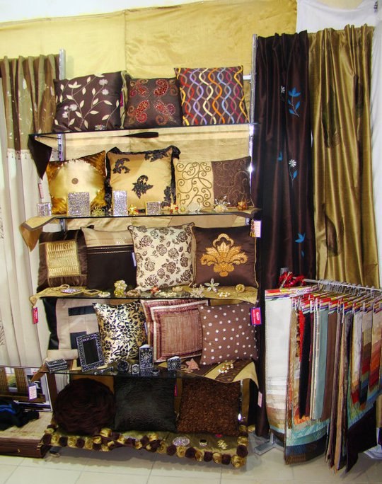 Showroom shelves with brown, gold and bronze pillow covers, embroidered florals and ruffle texture.